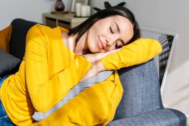 Evdeki oturma odasındaki kanepede dinlenen genç ve güzel bir kadın. Uyuyor ya da kestiriyor. Rahat kanepede dinlenen mutlu bir bayan. Refah ve refah kavramı.