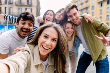 Genç bir grup mutlu insan dışarıda birlikte eğleniyor. Çok kültürlü öğrenci arkadaşlar seyahat tatilinin tadını çıkarırken selfie çekiyorlar. Gençlik toplumu ve arkadaşlık kavramı.
