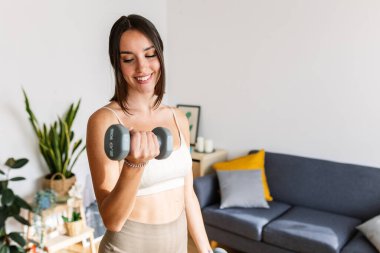 Atletik genç bayan evde dambıllarla egzersiz yapıyor. Spor ve spor konsepti