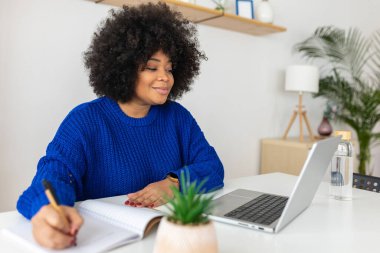Laptop görüntülerini dinleyen mutlu, genç bir kız öğrenci evde internetten ders çalışıyor. Eğitim ve e-öğrenim kavramı.