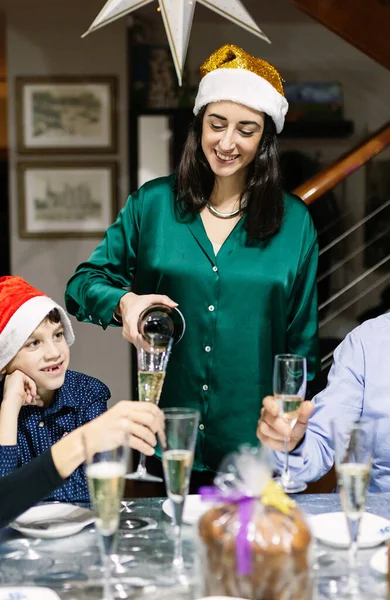 stock image Happy family celebrating christmas vacation at home. Young beautiful woman reunited with her family pours champagne into glass. New year and xmas concept. Vertical photo.