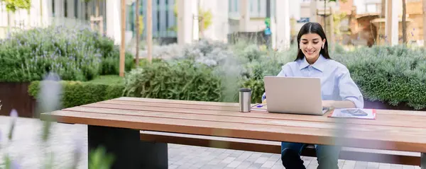 Young business woman studying master on laptop sitting outside of his office. Millennial adult student listening training online business class on computer. Banner aspect.
