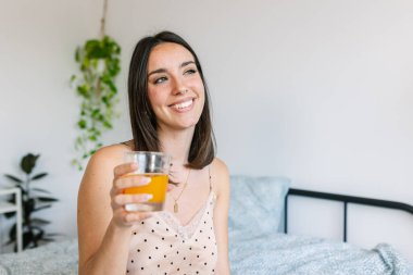 Yatakta pijamalı genç ve güzel bir kadın portakal suyu içiyor. Sağlıklı yaşam tarzı kavramı.