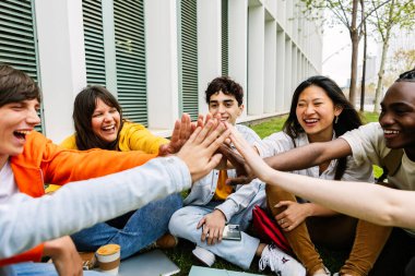 Üniversite kampüsünde el ele tutuşurken birbirlerine destek olan genç ve mutlu bir öğrenci grubu. Takım çalışması ve işbirliği kavramı.
