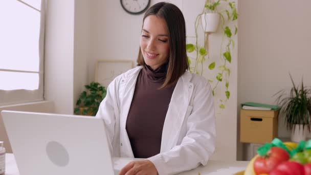 穿着白衣的女医生在写字台的笔记本电脑上工作 专业女从业人员在键盘上打字 看着诊所工作场所的电脑屏幕 保健人员概念 — 图库视频影像
