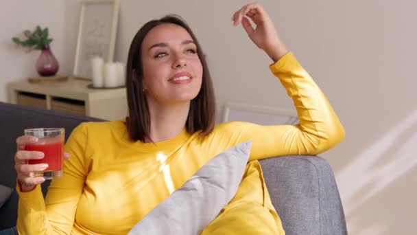 トマトジュースを飲んでいる間ソファーでリラックスして日光を楽しむ若い美しい女性 健康的なライフスタイルと幸福のコンセプト — ストック動画