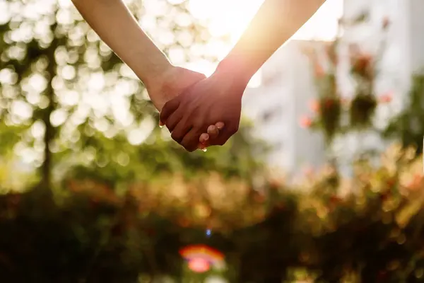Two unrecognizable young diverse women holding hands over city background. Close up rear view of lesbian couple standing together outdoors. Sunlight. Copy space