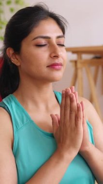 Huzurlu Hintli etnik kadının yoga minderinde oturduğu yakın plan görüntüsü. Ev stüdyosunda gözleri kapalı nefes alıp meditasyon yapıyor. Sağlıklı yaşam tarzı kavramı. Dikey görünüm videosu 9: 16