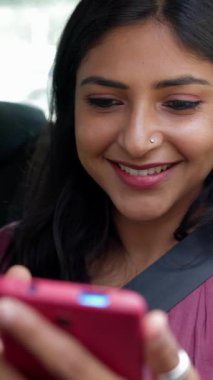 Bir arabanın arka koltuğunda cep telefonu kullanan mutlu genç Hintli kadın. Teknoloji ve ulaşım kavramı. Dikey görünüm videosu 9: 16