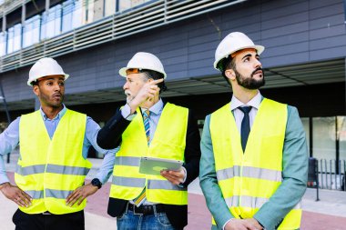 İnşaat alanında tartışırken dijital tablet kullanan üç inşaat mühendisi. Üst düzey mühendis, erkek mimar ve iş yatırımcısı ile proje detaylarını tartışan inşaat projesi.