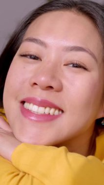 Evdeki kanepede uzanmış kameraya gülümseyen güzel Asyalı genç bir kadın. Sakinlik ve huzurlu ev hayatı anı konsepti. Dikey 9: 16 HD ekran görüntüsü.