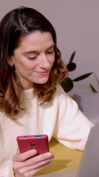 自宅で働いている間に携帯電話を使用してラップトップを持つ幸せな若い大人の女性 フリーランサービジネス起業家 テクノロジーライフスタイルコンセプト スクリーン映像 — ストック動画