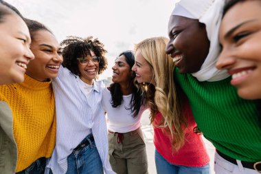 Farklı kültürlerden yedi mutlu genç kadın dışarıda birlikte gülüyor. Çeşitli kız arkadaş gruplarıyla kadın arkadaşlığı kavramı. Birbirlerine sarılıyorlar. Şehirde eğleniyorlar.