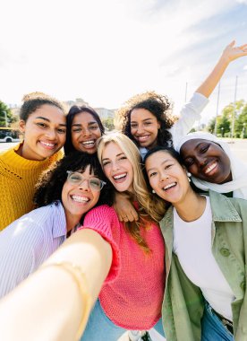 Çok ırklı yedi neşeli kadının selfie çekerken eğlendiği bir grup. Milenyum kızlarıyla kadın arkadaşlığı kavramı. Şehir caddesinde boş vakitlerin tadını çıkarıyorlar. Bütünleşme ve mutlu insanlar konsepti