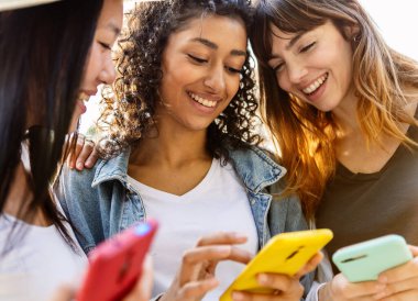 Şehirde cep telefonu kullanan üç mutlu güzel kadın. Milenyum kadın turist grubu akıllı telefon uygulamalarıyla sosyal medyanın tadını çıkarıyor. Teknoloji yaşam tarzı konsepti.