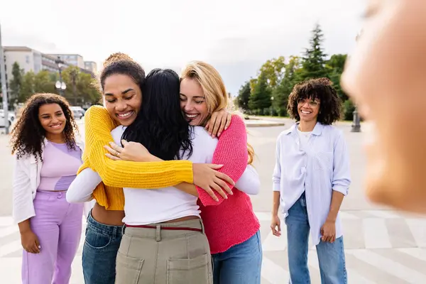 Happy multiracial women meeting together at city street, hugging each other. Millennial girls and female friendship concept.