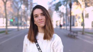 Şehir caddesinde duran neşeli genç bir kadının portresi. Şehirli arka planda kameraya gülümseyen mutlu beyaz kadın. Yüksek kalite 4k görüntü
