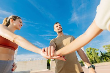 Bir grup genç sporcu arkadaş sokakta egzersiz yapmadan önce el ele tutuşup birbirlerini motive ediyorlar. Fitness, spor ve takım çalışması konsepti.