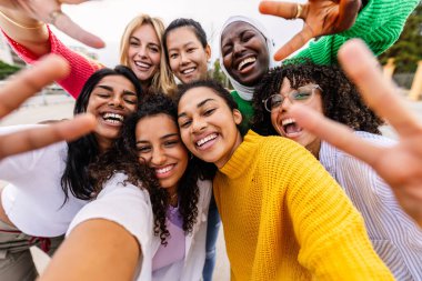 Çok ırklı genç bir kadın grubu selfie çektirip birlikte eğleniyorlar. Binlerce yıllık neşeli genç kızlar şehir caddesinde birlikte vakit geçiriyorlar. Kadın topluluğu ve arkadaşlık kavramı.