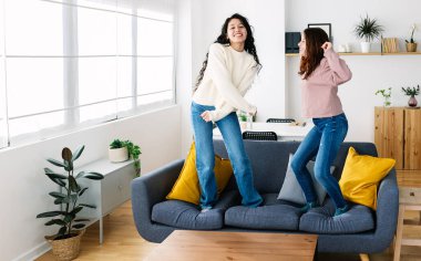 Evdeki kanepede dans eden iki mutlu bayan arkadaş. Ev arkadaşı ve ev arkadaşı kavramı.