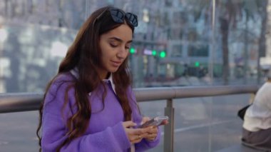 Tramvay istasyonunda bekleyen akıllı telefon kullanan mutlu genç bir kadın. Milenyum bayanı hücre ekranına bakıyor toplu taşıma durağında oturuyor. Şehir yaşam tarzı ve teknoloji konsepti.