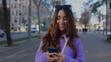 Şehir caddesinde cep telefonu kullanan güzel ve modaya uygun bir kız. Milenyum Latin Amerikalı kız öğrenci sosyal medya içeriğini şehir geçmişi üzerinden izliyor. Cep telefonuyla konuşan bir kadın..