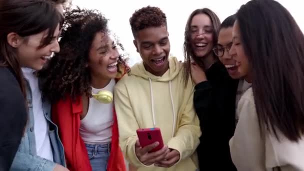 スマートフォンで面白いビデオを見ながら一緒に笑う多様な学生の友人が幸せです ソーシャルメディアモバイルアプリを使用して楽しんでいる若い多民族 — ストック動画
