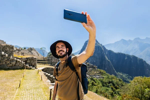 Machu Picchu 'da fotoğraf makinesiyle selfie çeken genç bir adam. Güney Amerika, Peru 'da tatilin tadını çıkaran neşeli erkek turist. Seyahat ve tatil kavramı.