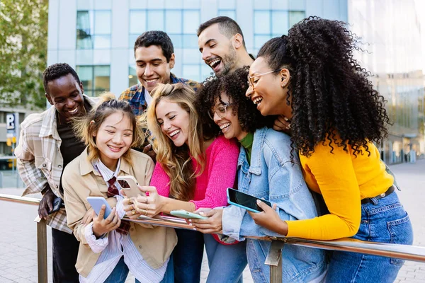 Young group of happy people smiling while using mobile phone at city street. Multiracial diverse friends standing over urban background holding cellphones. Technology, youth and social media concept