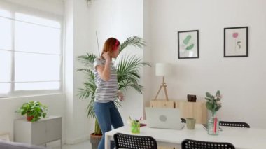 Neşeli genç bir kadın, kablosuz kulaklıkla müzik dinliyor, oturma odasında dans ediyor, işe ya da derslere ara veriyor. Mutlu insanlar ve tasasız konsept.