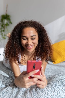 Sabahları yatağında cep telefonu kullanan mutlu Latin kız. Teknoloji ve sosyal medya kavramı