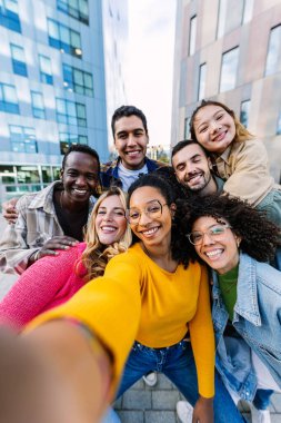 Genç yetişkin arkadaşlar selfie grup portresindeki telefon kamerasına gülümsüyor. Gençlik cemiyeti konsepti neşeli bin yıllık öğrencilerle birlikte şehir sokaklarında eğleniyor..