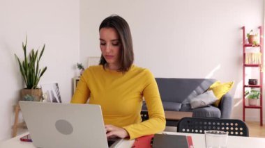 Oturma odasında dizüstü bilgisayarla çalışan mutlu bin yıllık kadın. Evdeki masada bilgisayar kullanarak öğrenen güzel bir kız öğrenci. E-öğrenim ve iş konsepti