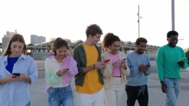 Genç bir grup insan dışarıda yürürken cep telefonlarını birlikte kullanıyor. Teknoloji yaşam tarzı, sosyal medya ve gençlik kavramı.
