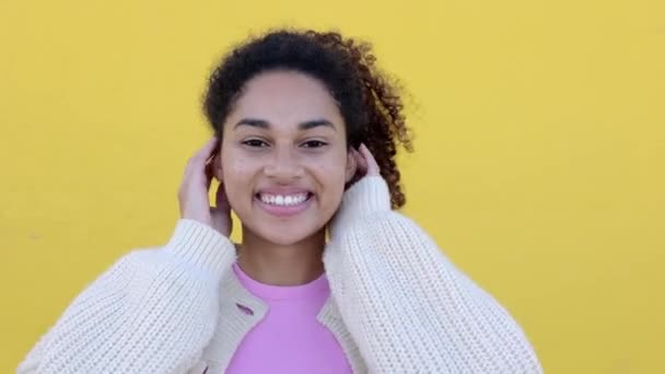 陽気な若いラテンアメリカ人女性が黄色い背景のカメラで微笑んでいる カーリーガールの肖像画がポジティブで 外に微笑みを浮かべる — ストック動画
