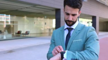 Profesyonel genç iş adamı dışarıda dikilirken saati kontrol ediyor..