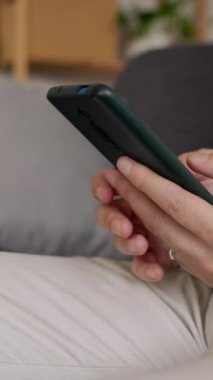 Profesyonel iş adamı işten sonra evdeki koltukta otururken cep telefonu kullanıyor. Kanepede hücrede dinlenirken çevrimiçi mesaj yazan tanınmayan kişi. Dikey 9: 16 görünüm görüntüsü.