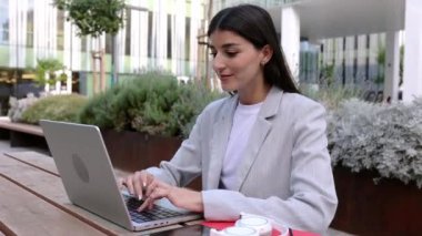 Genç başarılı iş kadını laptopta çalışıyor açık havada şirket binasının masasında oturuyor. İş hayatı ve girişimci insan kavramı.