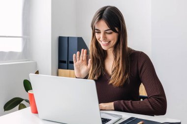 Genç mutlu kadın dizüstü bilgisayarla el sallıyor. Milenyum kadınlarının internetten öğrenmesi. Eğitim ve iş konsepti.