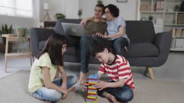 Çocuklar evdeki oturma odasında dizüstü bilgisayar kullanırken yerde birlikte oynuyorlar. Çocukluk ve aile kavramı.