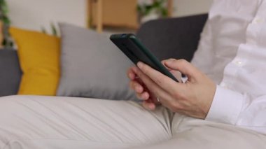 Profesyonel iş adamı işten sonra evdeki koltukta otururken cep telefonu kullanıyor. Kanepede hücrede dinlenirken çevrimiçi mesaj yazan tanınmayan kişi. Teknoloji konsepti.