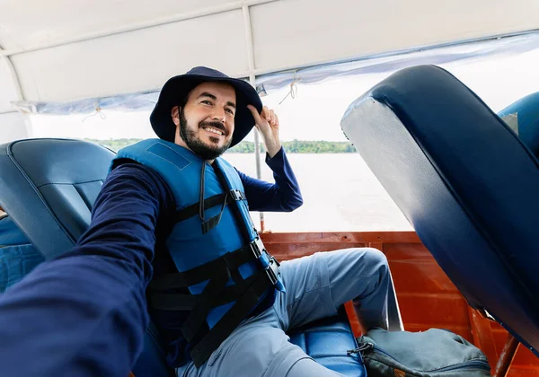 Young adventurer man taking a selfie portrait with cellphone while sailing on fast boat on the Amazon River in Peru, South America. Travel and vacation concept.