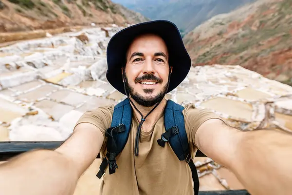 Happy young tourist man taking selfie portrait at salt terrace in Maras, Peru. Travel and holidays concept