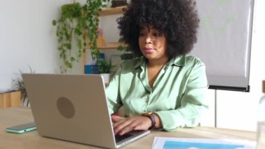 Profesyonel Latin Amerikalı iş kadını ofis içinde dizüstü bilgisayarla çalışıyor. Gülümseyen Afro-Amerikan kadın çalışan şirket grafik büyümesini analiz ediyor.