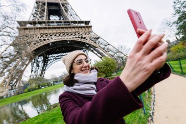 Arka planda Paris Eyfel Kulesi ile selfie portresi çekmek için cep telefonu kullanan mutlu genç turist kadın. Seyahat ve tatil kavramı.