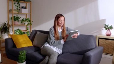Dijital cihazda sosyal medya içeriğini izleyen bin yıllık beyaz bir kadın. Evdeki kanepede dinlenirken dijital tablet kullanan güzel genç bir kadın..
