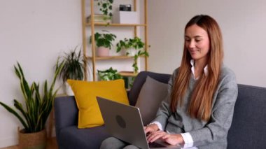 Kanepede dizüstü bilgisayar kullanan mutlu bir kadın. Milenyum dişisi evden bilgisayarda çalışıyor, internetten okuyor ya da internette geziniyor..