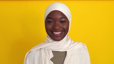 Beyaz Müslüman türbanlı mutlu genç Afrikalı kadının portresi sarı stüdyo arka planında kameraya gülümsüyor. Mutluluk ve iyi titreşimler konsepti.