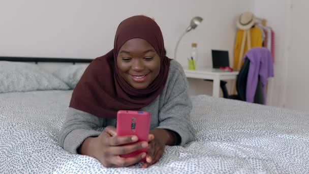 ハッピーブラックイスラム教徒の女性ヒジャブは 自宅でベッドでリラックスしたスマートフォンを使用しています 高品質の4K映像 — ストック動画