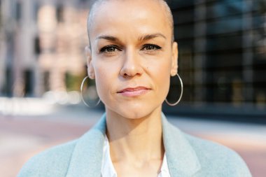 Yetişkin bir iş kadınının, kentsel arka planda kendine güvendiğini gösteren kameraya bakması. İş adamları ve güçlendirme kavramı.